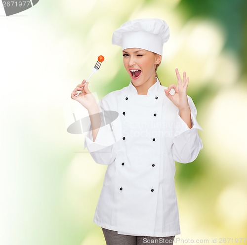 Image of smiling female chef with fork and tomato