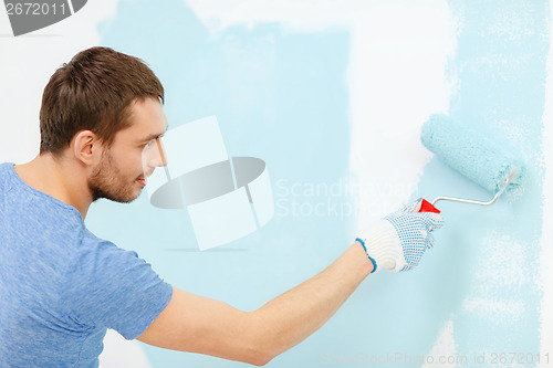 Image of smiling man painting wall at home