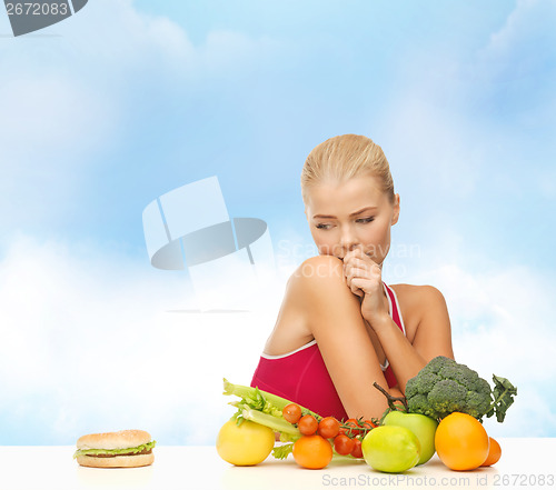 Image of doubting woman with fruits and hamburger