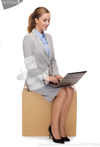 Image of smiling woman sitting on cardboard box with laptop