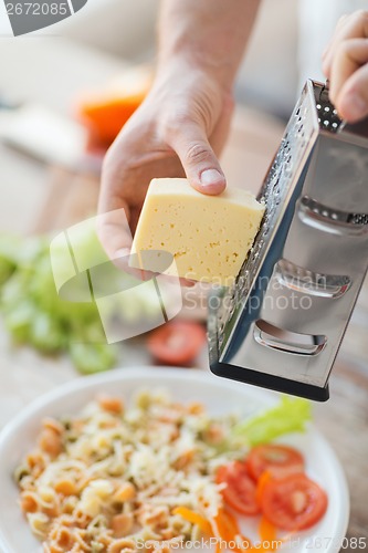 Image of close up of male hands grating cheese over pasta