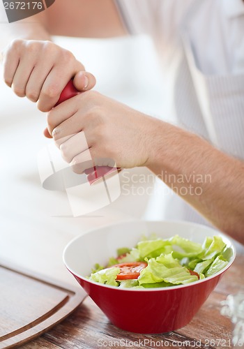 Image of close up of male hands flavouring salad in a bowl