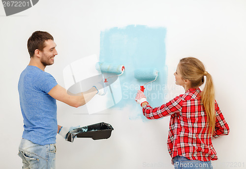 Image of smiling couple painting wall at home