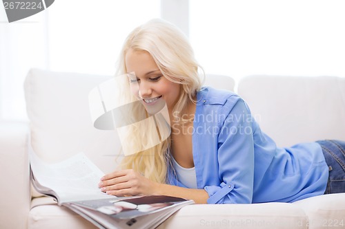 Image of woman lying on couch and reading magazine at home