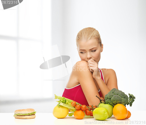 Image of doubting woman with fruits and hamburger