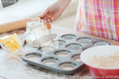 Image of close up of hand filling muffins molds with dough