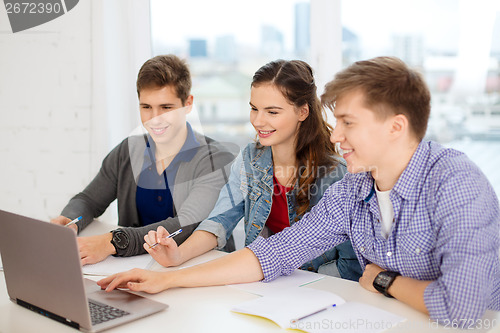 Image of three smiling students with laptop and notebooks