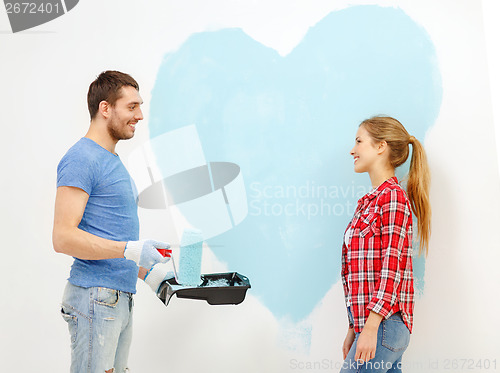 Image of smiling couple painting big heart on wall