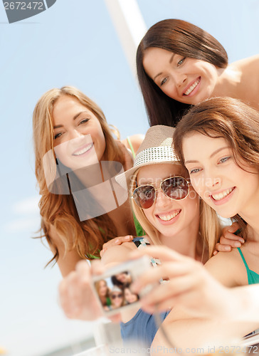 Image of smiling girls taking photo in cafe on the beach