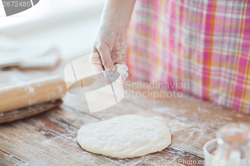 Image of closeup of female hand sprinkling dough with flour