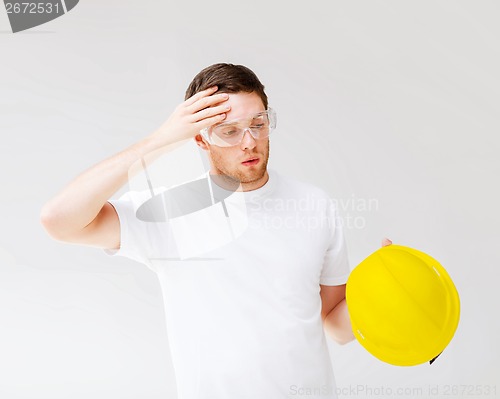 Image of male builder in safety glasses taking off helmet