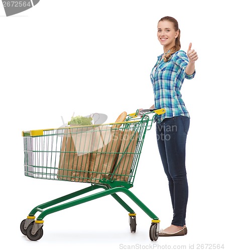 Image of smiling young woman with shopping cart and food