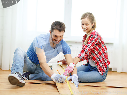 Image of smiling couple measuring wood flooring