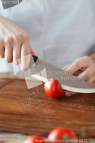Image of male hand cutting tomato on board with knife