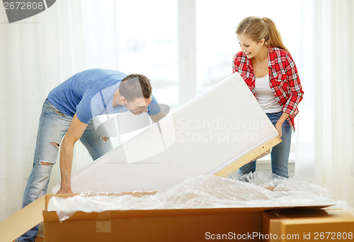 Image of smiling couple opening big cardboard box with sofa