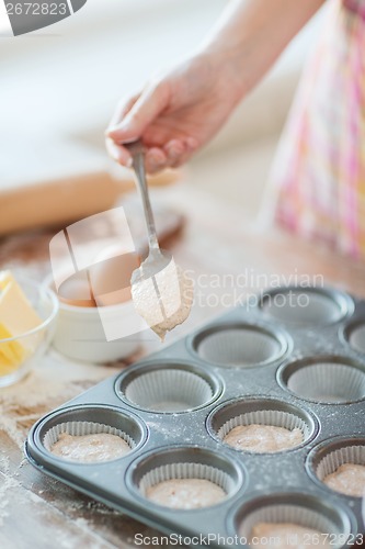 Image of close up of hand filling muffins molds with dough