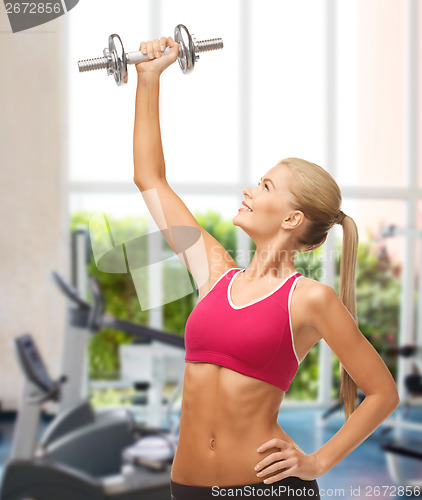 Image of smiling woman lifting steel dumbbell at gym