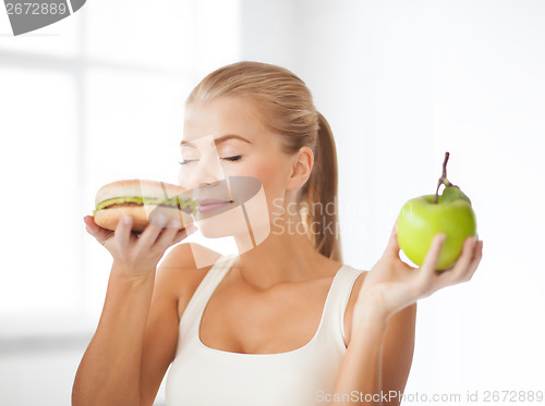 Image of smiling woman smelling hamburger and holding apple