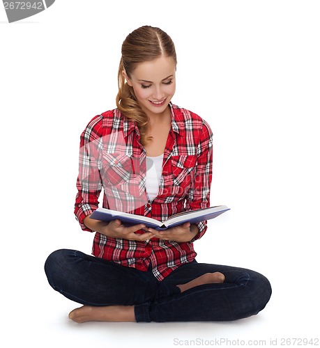 Image of smiling young woman sittin on floor with book