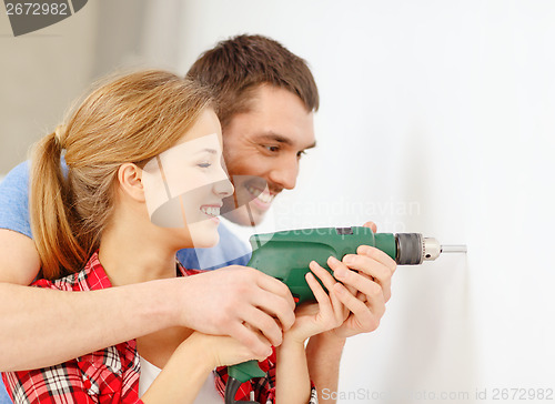 Image of smiling couple drilling hole in wall at home