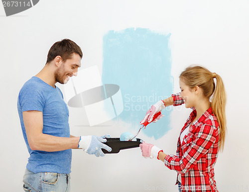 Image of smiling couple painting wall at home