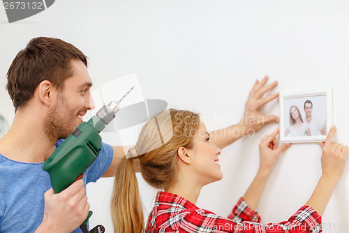 Image of smiling couple drilling hole in wall at home