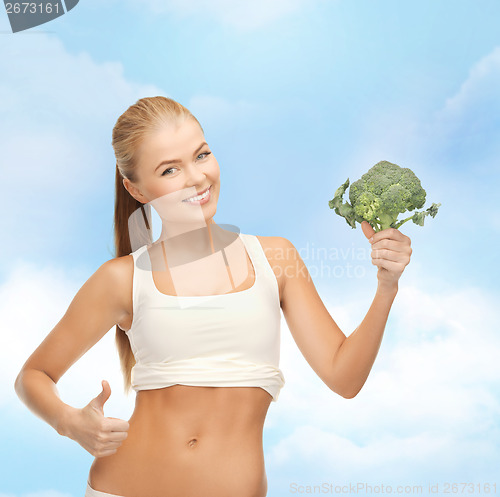 Image of woman pointing at her abs and holding broccoli