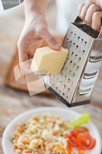 Image of close up of male hands grating cheese over pasta