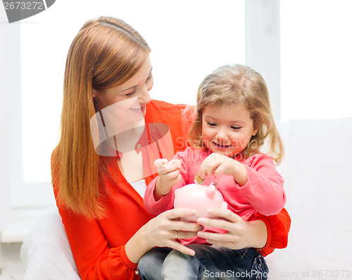 Image of happy mother and daughter with small piggy bank