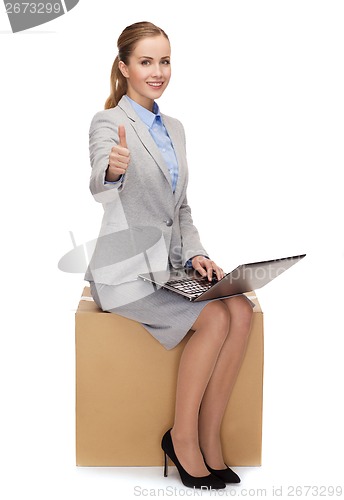 Image of smiling woman sitting on cardboard box with laptop