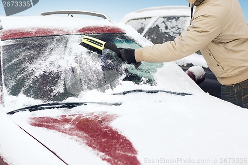 Image of man cleaning snow from car windshield with brush