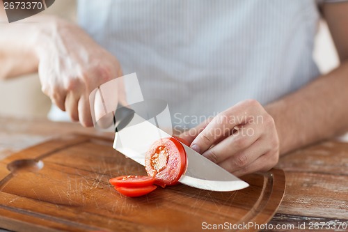 Image of male hand cutting tomato on board with knife