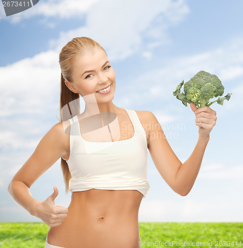 Image of woman pointing at her abs and holding broccoli