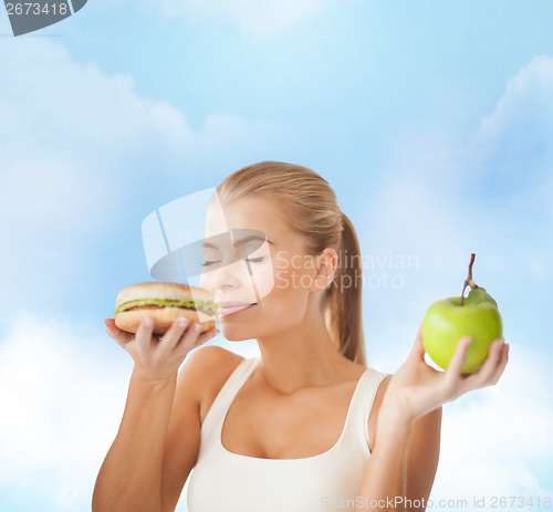 Image of happy woman smelling hamburger and holding apple
