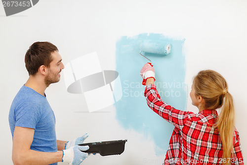 Image of smiling couple painting wall at home