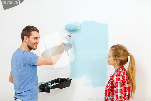 Image of smiling couple painting wall at home