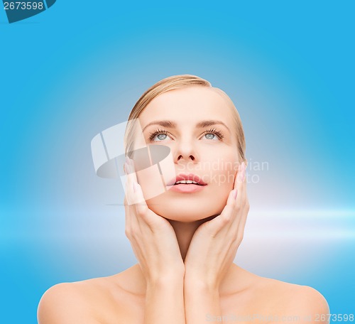Image of beautiful woman touching her face and looking up
