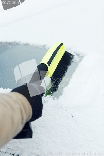 Image of man cleaning snow from car windshield with brush