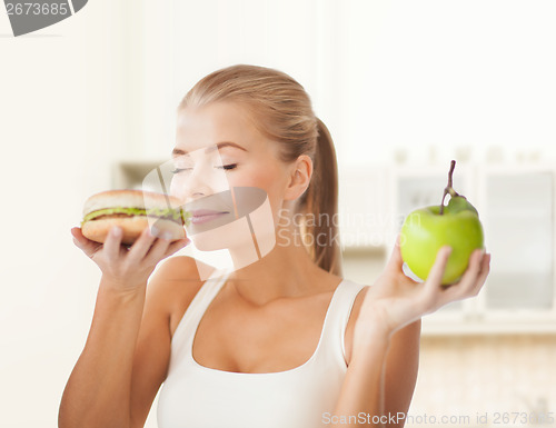Image of happy woman smelling hamburger and holding apple