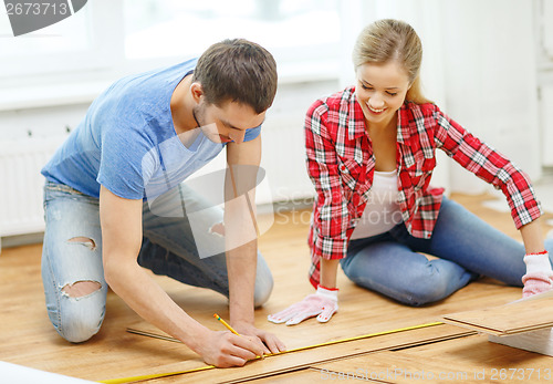 Image of smiling couple measuring wood flooring