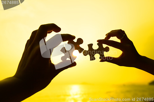 Image of Two hands trying to connect puzzle pieces with sunset background