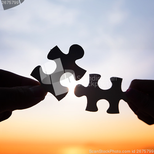 Image of Two hands trying to connect puzzle pieces 