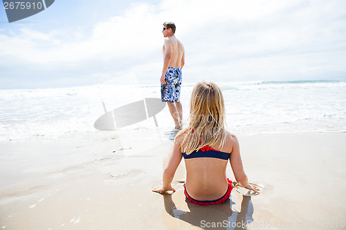 Image of Young girl sitting on sand at beach watching father