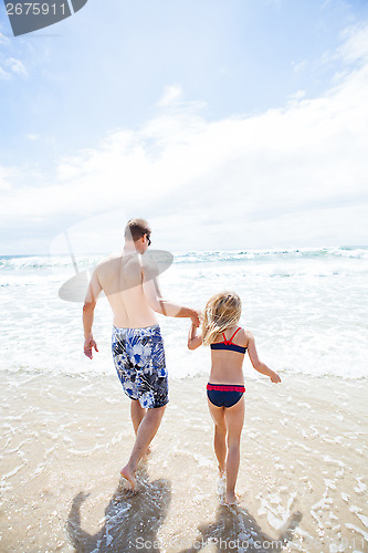 Image of Father and young daughter walking into water at beach