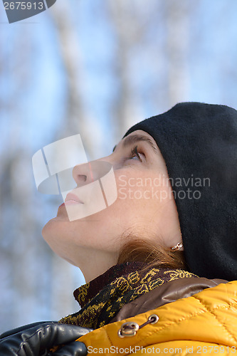 Image of Woman in black beret and a yellow jacket with a hood. Looking up.