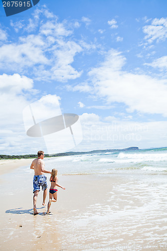 Image of Father and young daughter running along beach