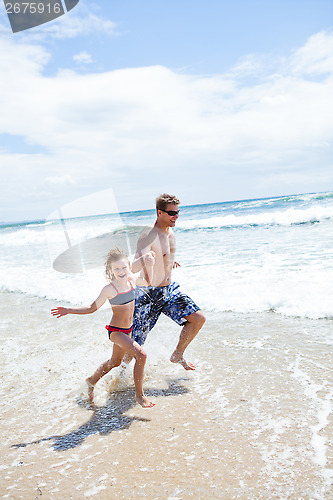 Image of Happy father and daughter running along beach in shallow water
