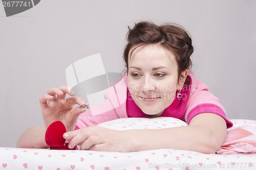 Image of girl holds a gift ring, lying in bed