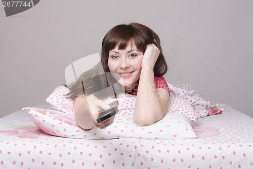 Image of Girl with remote control in bed watching TV