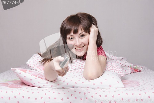 Image of Happy girl with the remote in bed watching TV